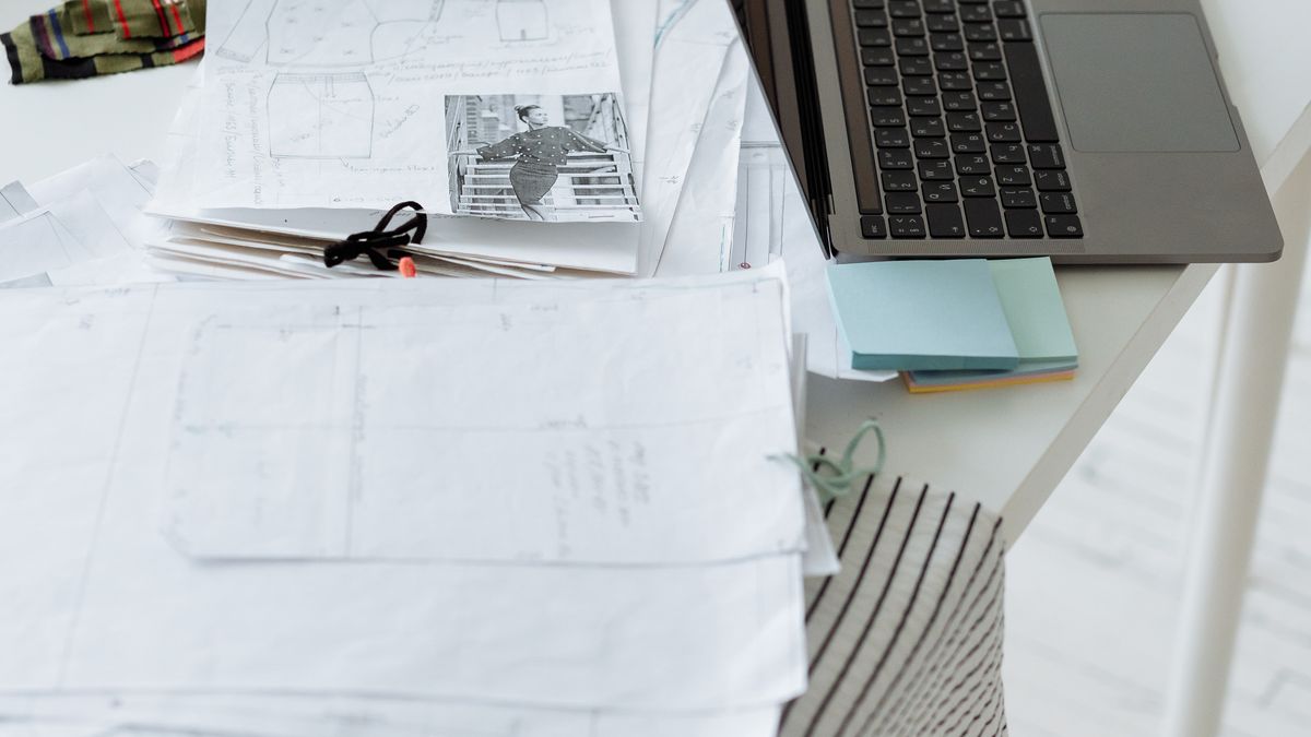 A laptop beside paper sketches on a work table