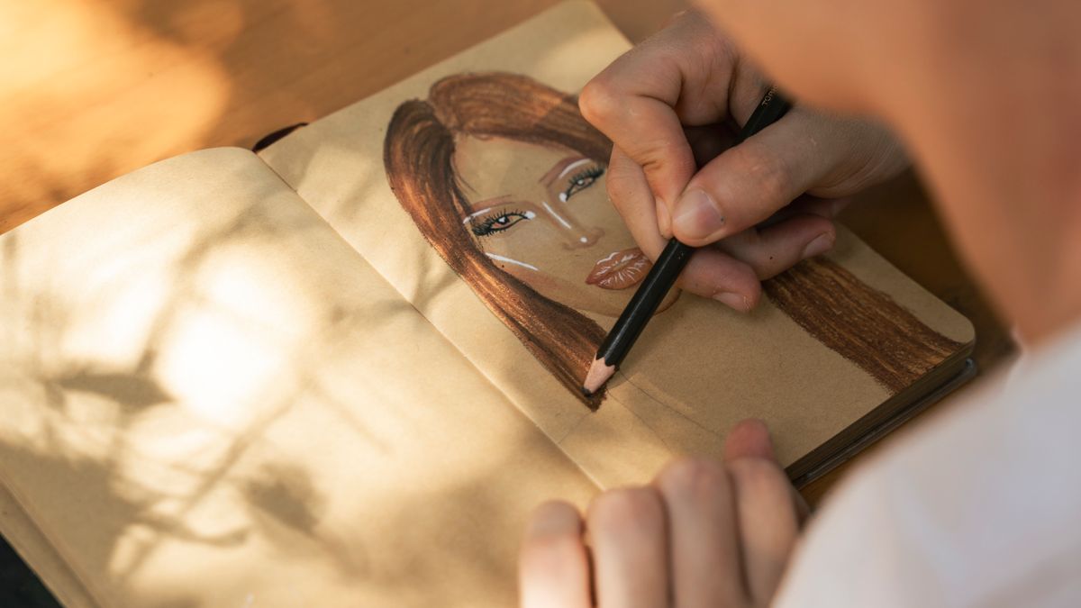 An artist using pencils to draw a portrait in a sketchbook