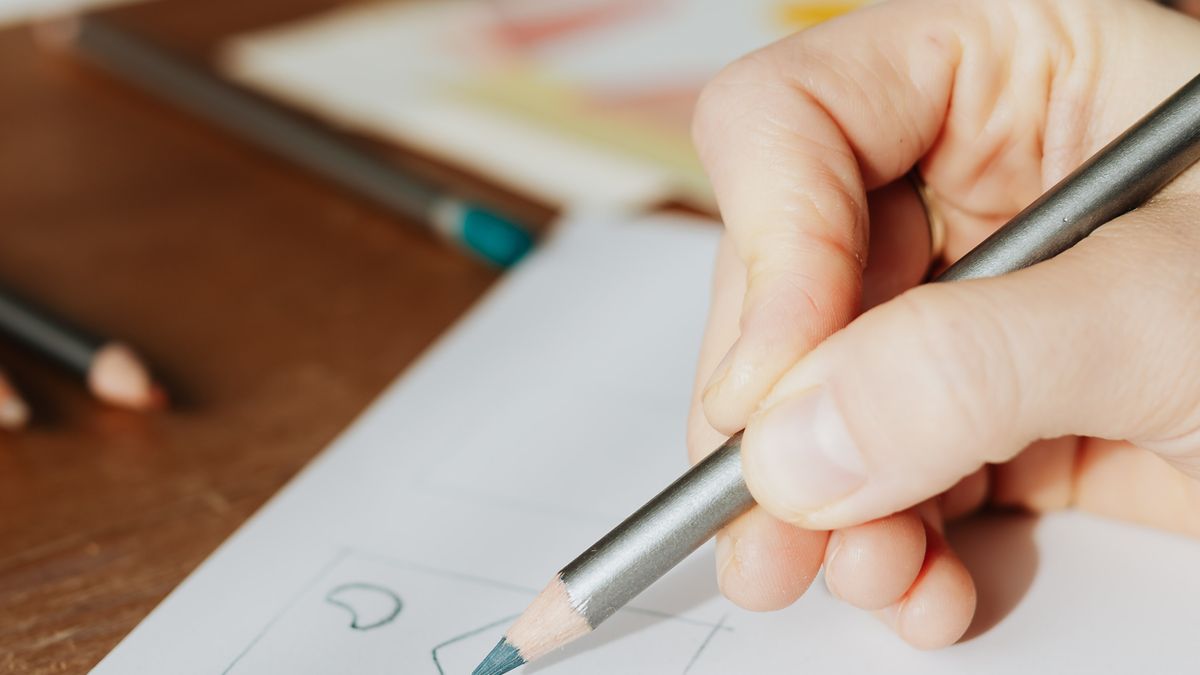 A hand drawing pencil sketches on paper at a desk