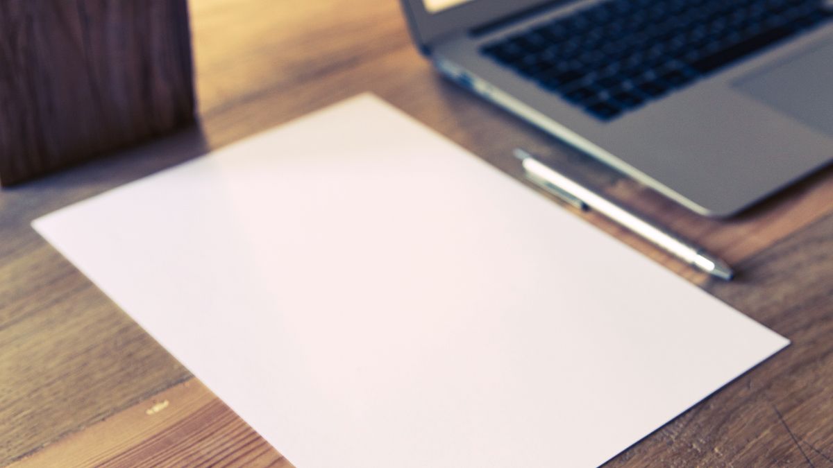 A laptop, blank paper and pen on a wooden desk